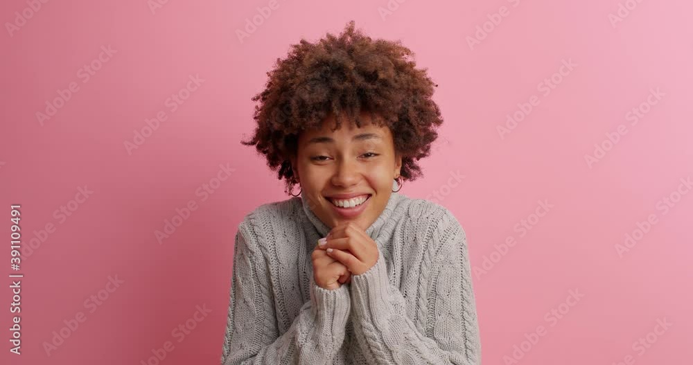 Beautiful cheerful woman clasps hands then smiles and looks with admiration at something satisfied by pleasant thing dressed in knitted sweater poses against rosy background. Happy feelings concept Beautiful cheerful woman clasps hands then smiles and looks with admiration at something satisfied by pleasant thing dressed in knitted sweater poses against rosy background. Happy feelings concept