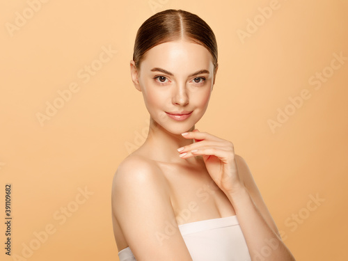 Young beautiful woman with brown eyes and perfect skin, touching her chin, isolated on beige background