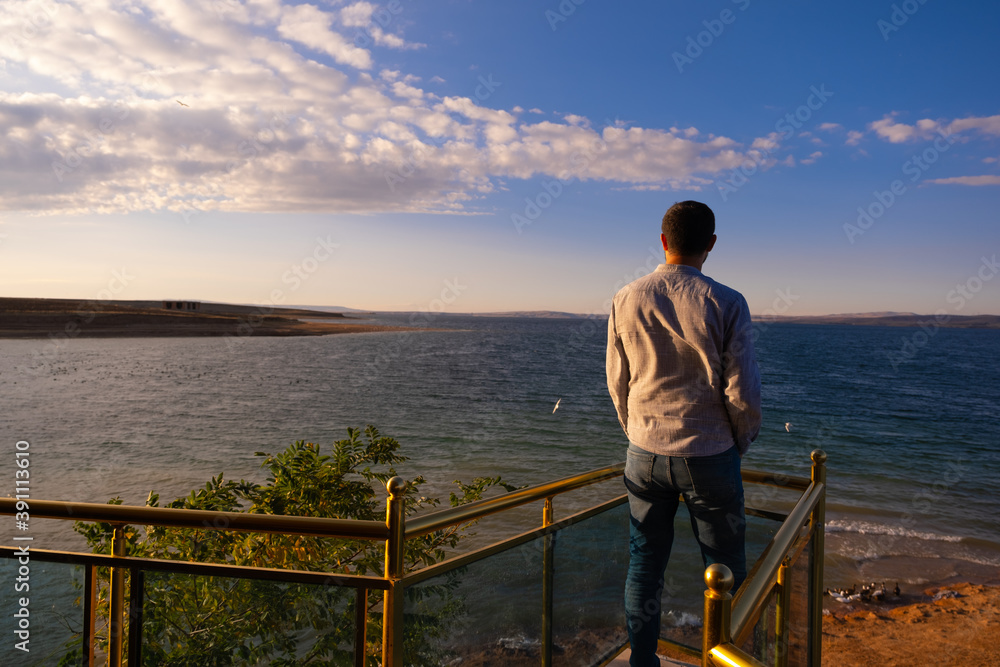 man watching the view by the sea. his hands in his pockets. blue sky with clouds.