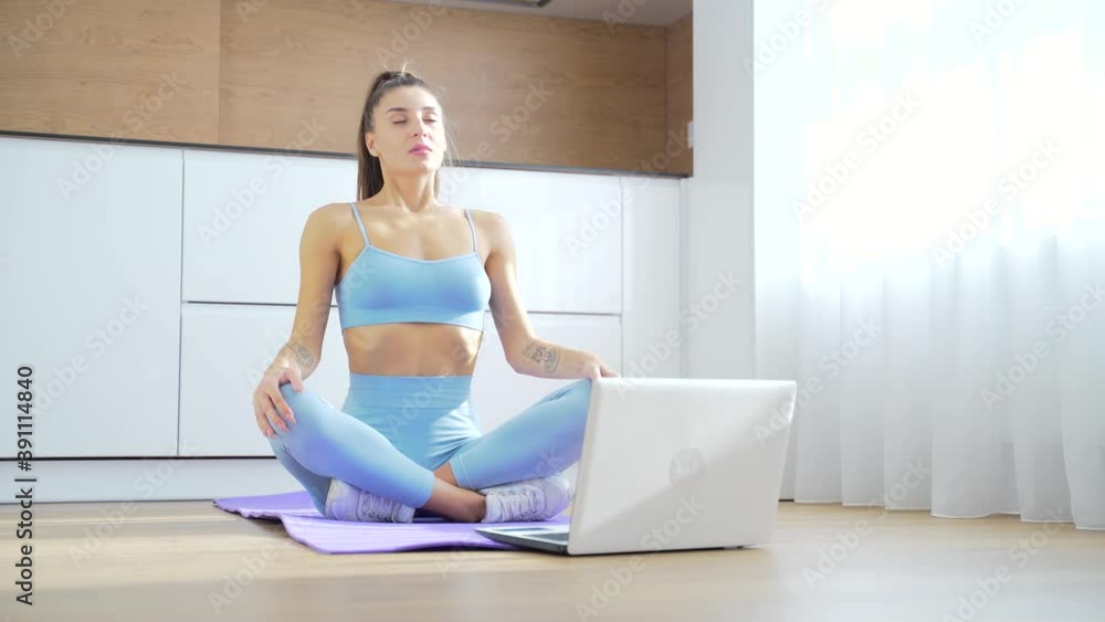 young fitness woman in sportswear doing yoga exercises online in front of laptop in kitchen sitting on the floor. girl goes sports a distance on lessons during quarantine at home. Distance training. young fitness woman in sportswear doing yoga exercises online in front of laptop in kitchen sitting on the floor. girl goes sports a distance on lessons during quarantine at home. Distance training.