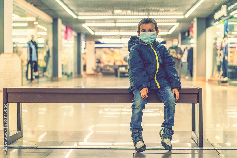 Obraz premium Toddler child, boy, wearing protective medical mask in shopping center during coronavirus Covid 19 pandemic. The child wears a protective mask in the store. toned