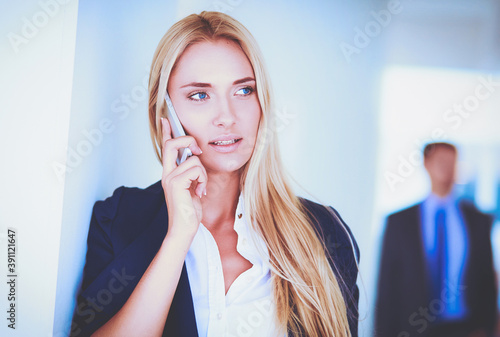 Businesswoman standing against office window talking on mobile phone