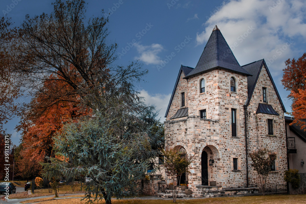 Three story rock house with tower in Autumn with pretty foliage and trees parked along the road