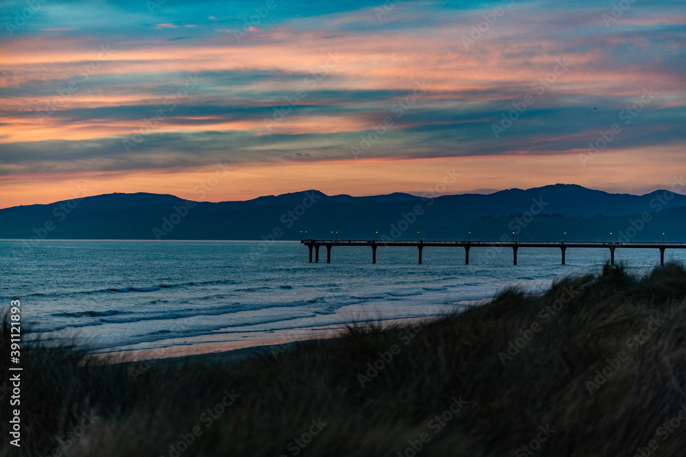 Sunset at the coast with a pier in New Zealand Sunset at the coast with a pier in New Zealand