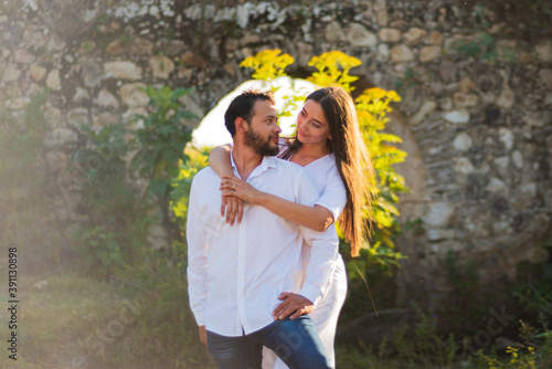 A romantic and lovely latin couple dressed in white with the ruins of a stone bridge behind and a beautiful sunset in  the background photo