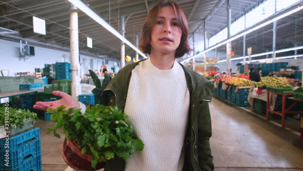 A woman blogger holds a basket of vegetables on her hand. Speaks information to subscribers from the farmers market. Takes steps.