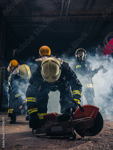 Group of three young fireman posing inside the fire department with uniform and tools © qunica.com