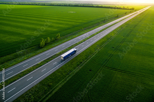 blue truck driving on asphalt road along the green fields. seen from the air. Aerial view landscape. drone photography.  cargo delivery
