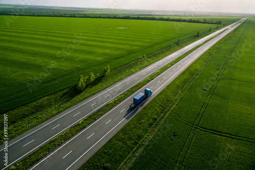 blue truck with container driving on asphalt road among the green fields. seen from the air. Aerial view landscape. drone photography. cargo delivery