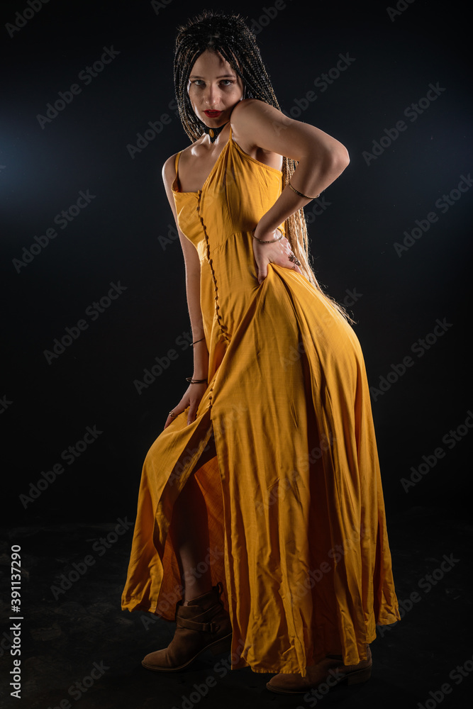 Mystic ancient queen goddess wearing a yellow dress on an isolated black studio background. Female feminist wearing braids and posing in a studio.