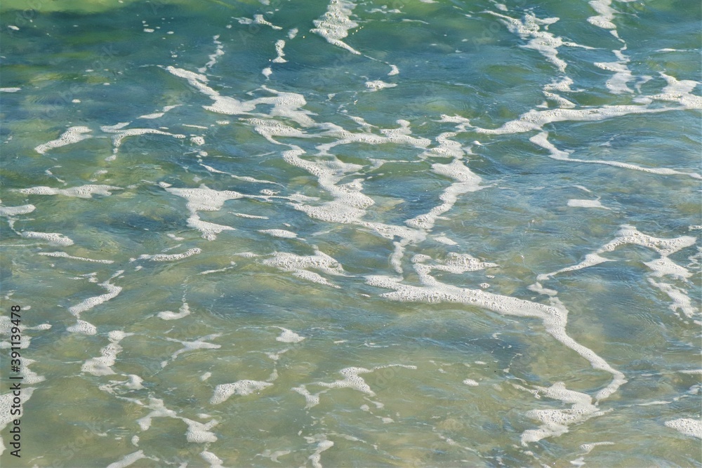 On the beach - ocean water, yellow sand, white foam on the water, close-up On the beach - ocean water, yellow sand, white foam on the water, close-up