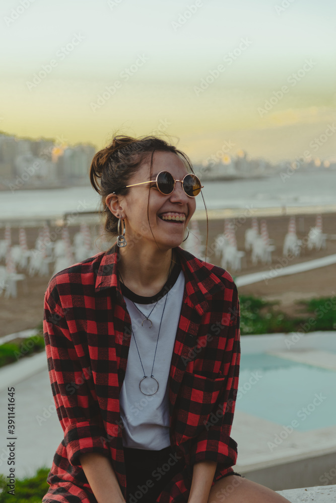 Young beautiful brunette woman in casual red plaid shirt outdoors in the city, beach background, travel campaign, fashion concept, happy woman, copy space, social media, urban style Young beautiful brunette woman in casual red plaid shirt outdoors in the city, beach background, travel campaign, fashion concept, happy woman, copy space, social media, urban style