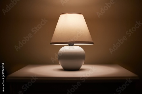Small lamp glowing in bedroom night stand, close up, dim room