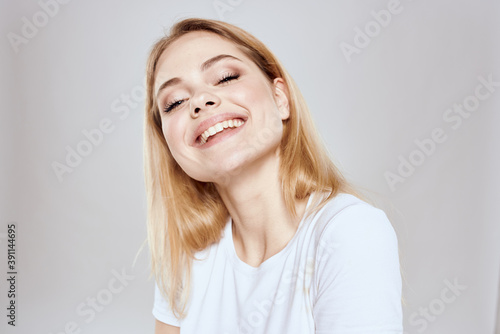 cheerful blonde in a white t-shirt gesturing with her hands light background © SHOTPRIME STUDIO
