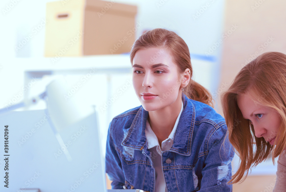 Obraz premium Two young woman standing near desk with instruments, plan and laptop.