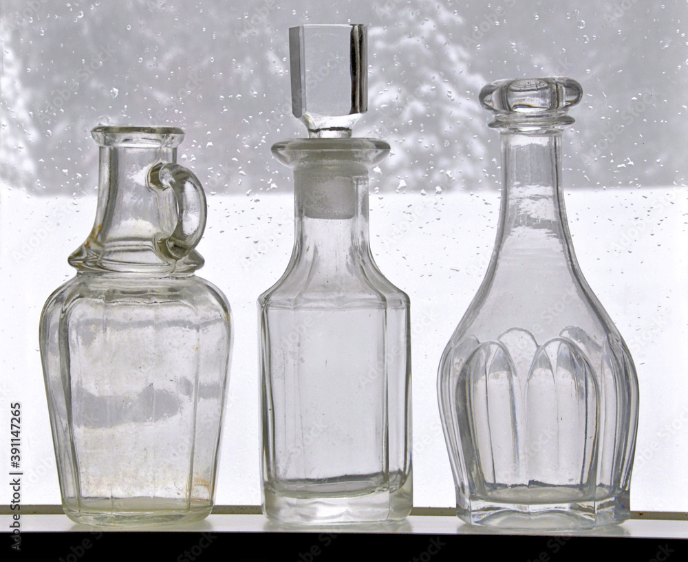 Seasonal still life. Collection of old empty bottles (two with glass stoppers) displayed in window with winter scene outdoors and drops of melted snow on surface of glass. Seasonal still life. Collection of old empty bottles (two with glass stoppers) displayed in window with winter scene outdoors and drops of melted snow on surface of glass.