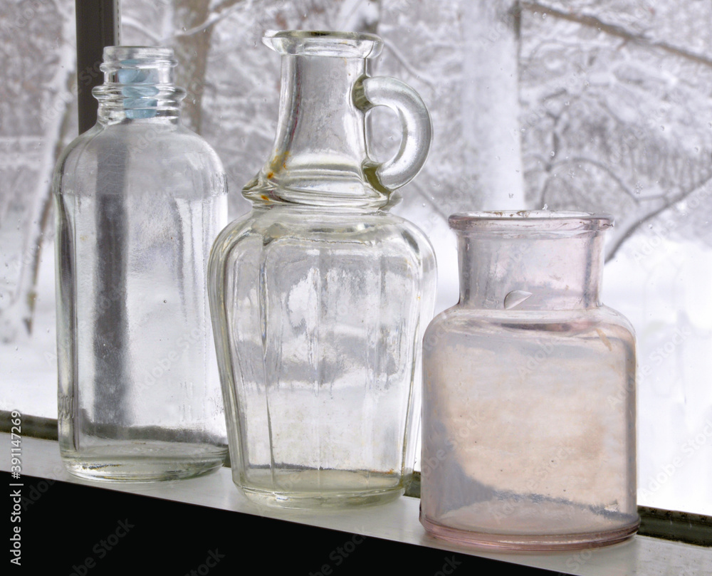 Seasonal still life. Closeup of three old empty bottles displayed in window with view of winter snow scene outdoors.