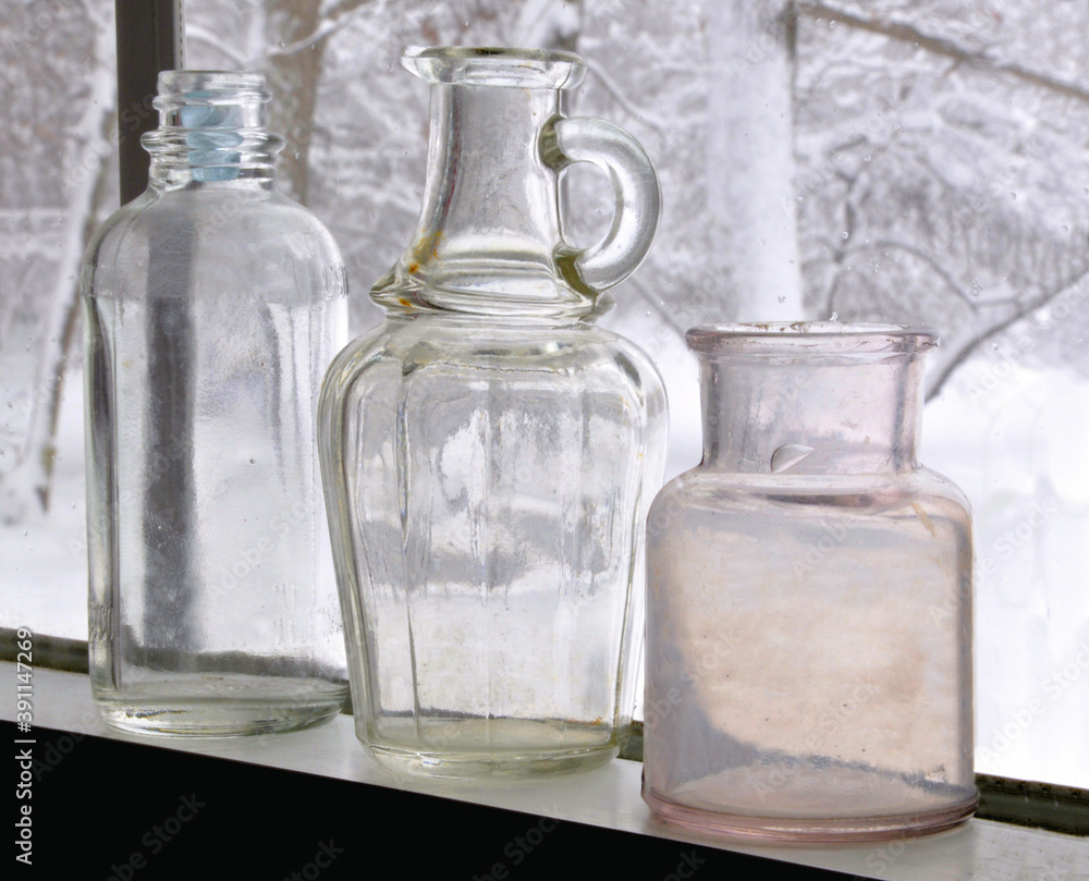 Seasonal still life. Closeup of three old empty bottles displayed in window with view of winter snow scene outdoors. Seasonal still life. Closeup of three old empty bottles displayed in window with view of winter snow scene outdoors.