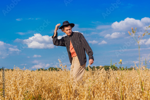 Tall handsome man with black hat standing at golden oat field. © Smile