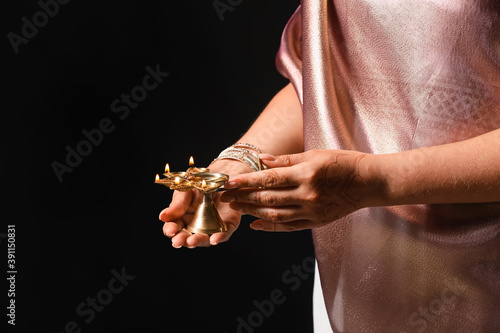 Woman holding diya lamp for celebration of Divaly on dark background, closeup © Pixel-Shot