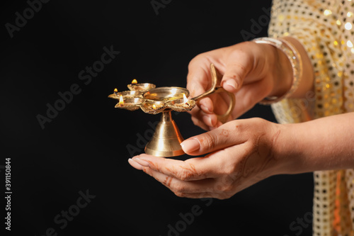 Woman holding diya lamp for celebration of Divaly on dark background, closeup