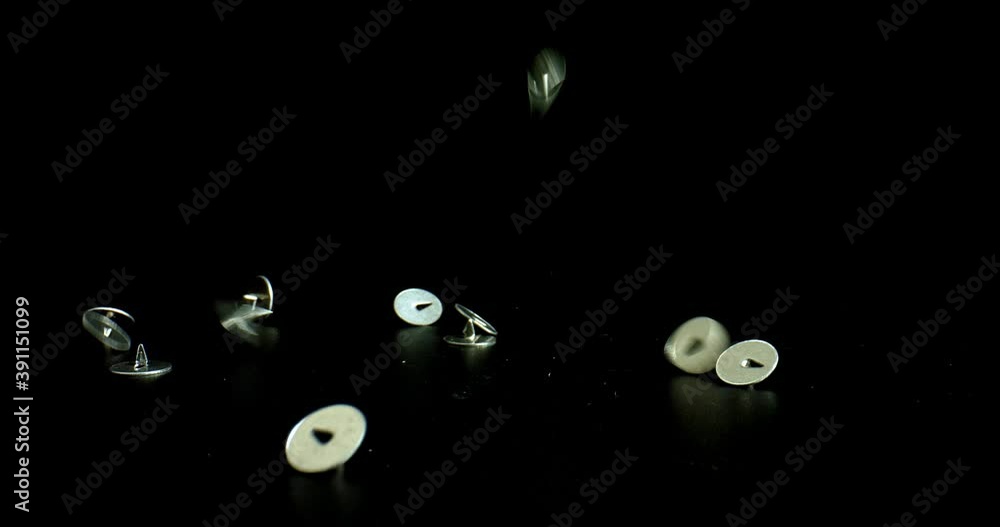 Metal Push Pins falling in slow motion on black reflective surface. Buttons shimmers in the light. Office routine concept Metal Push Pins falling in slow motion on black reflective surface. Buttons shimmers in the light. Office routine concept