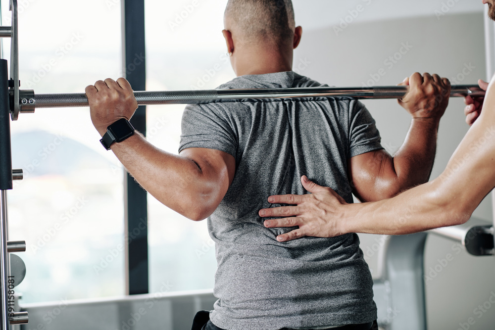 Fitness trainer asking client to keep back straight when doing squats with barbell Fitness trainer asking client to keep back straight when doing squats with barbell