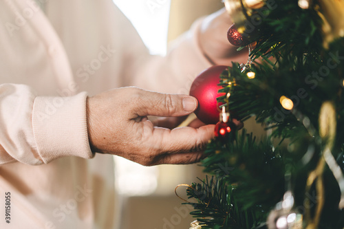 Close up elder woman hand decor Christmas tree at home.