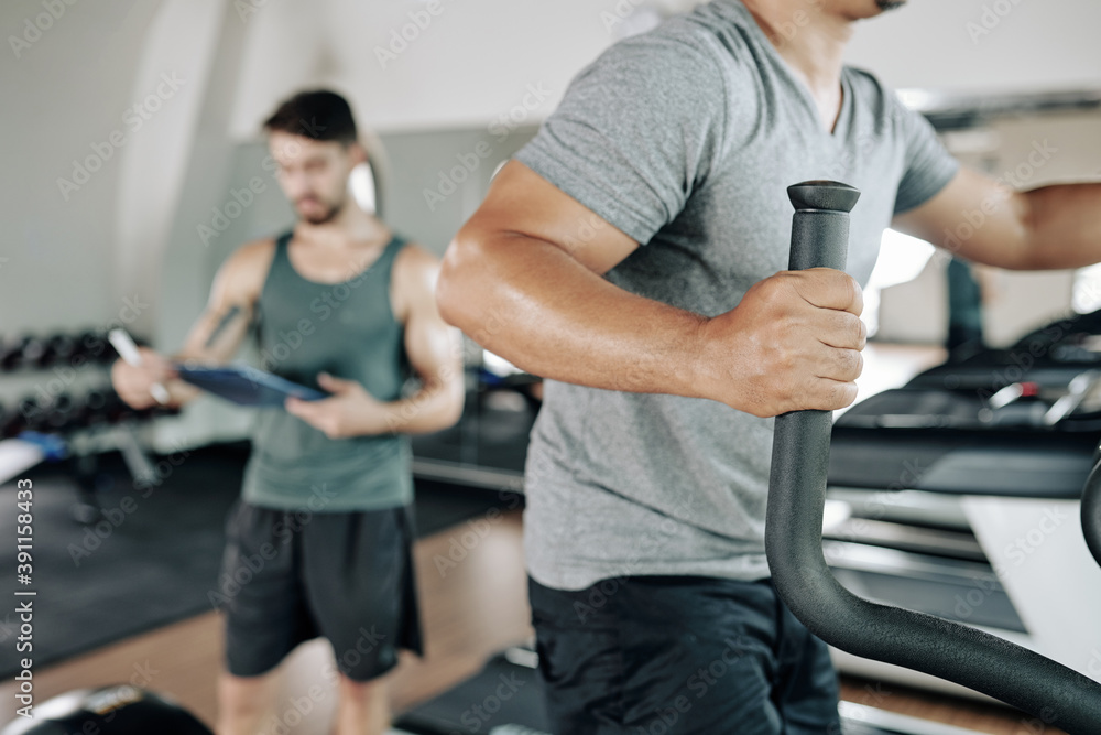 Close-up image of fit man warming up in elliptical machine before working out in gym
