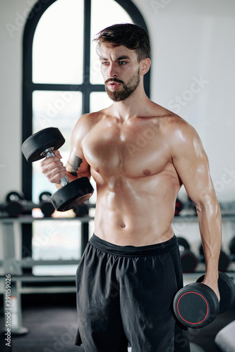 Handsome strong muscular man lifting dumbbells when standing in gym