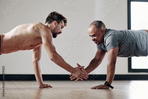 Strong men giving each other high five when standing in plank position on gym floor
