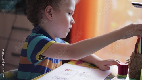 Little boy draws at a table at home. The child is engaged in creativity, studying at home, video