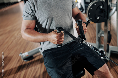 Cropped image of strong man doing exercise in row machine in gym