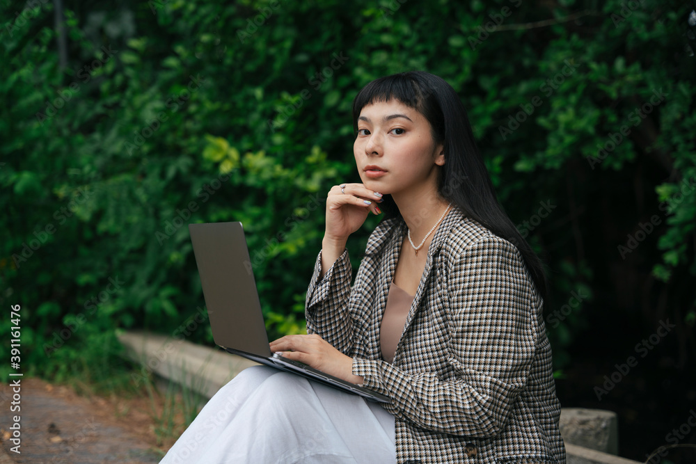 Asian woman in formal shirt using computer laptop outdoors. Asian woman in formal shirt using computer laptop outdoors.
