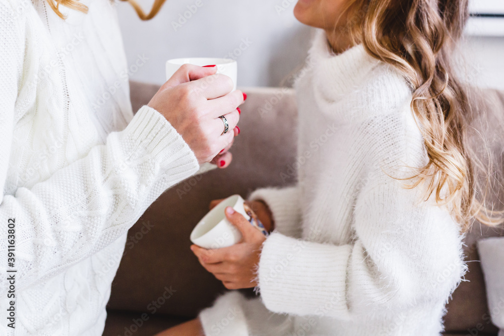 Mother and daughter in light sweaters are sitting on the sofa, the room is decorated for the new year and Christmas, hugs, conversations, smiles, kisses, waiting for a gift and magic Mother and daughter in light sweaters are sitting on the sofa, the room is decorated for the new year and Christmas, hugs, conversations, smiles, kisses, waiting for a gift and magic