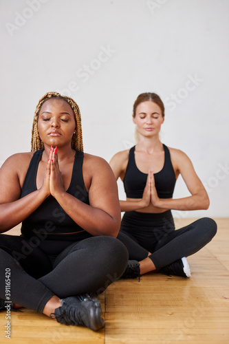 calm afro american and caucasian women in sportswear meditating, keep calm sitting on the floor, sit with eyes closed