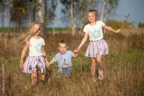 Foto Happy family: sisters and little brother on a summer meadow.