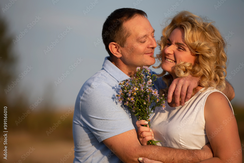 Beautiful middle-aged couple in love hugging on the background of nature.