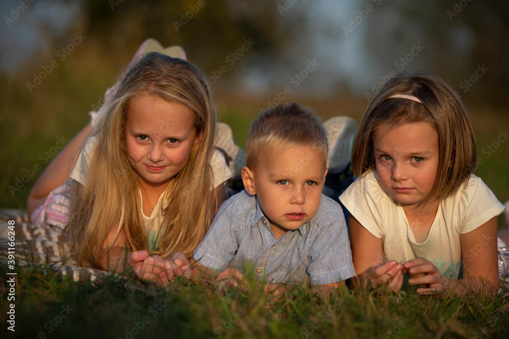 Sisters and little brother lie on the grass. Children play in the meadow. A happy family. Sisters and little brother lie on the grass. Children play in the meadow. A happy family.
