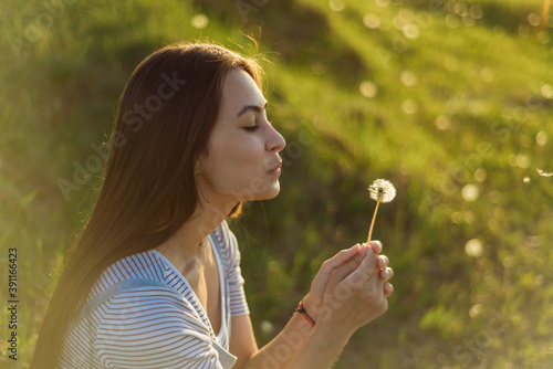 Happy young woman blows on a dandelion in an open field in the sun. the concept of lightness  freedom and happiness