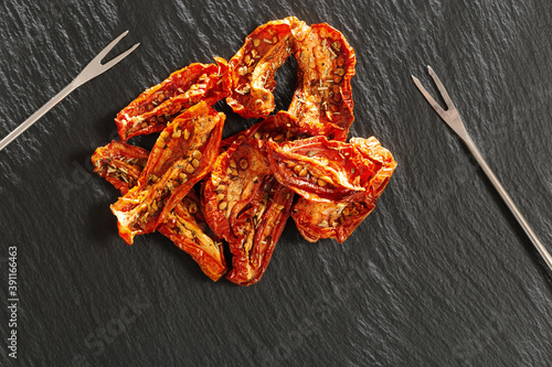 Sun dried tomatoes slices with Italian herbs and spices on dark background. Homemade dehydrated vegetable.