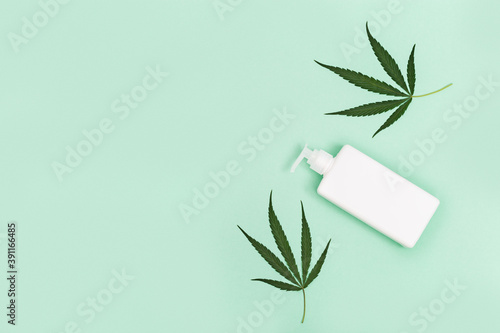 Jar with cosmetic product,  gel or shampoo with cannabis oil on green colored background. White flack for self-care. View from above.