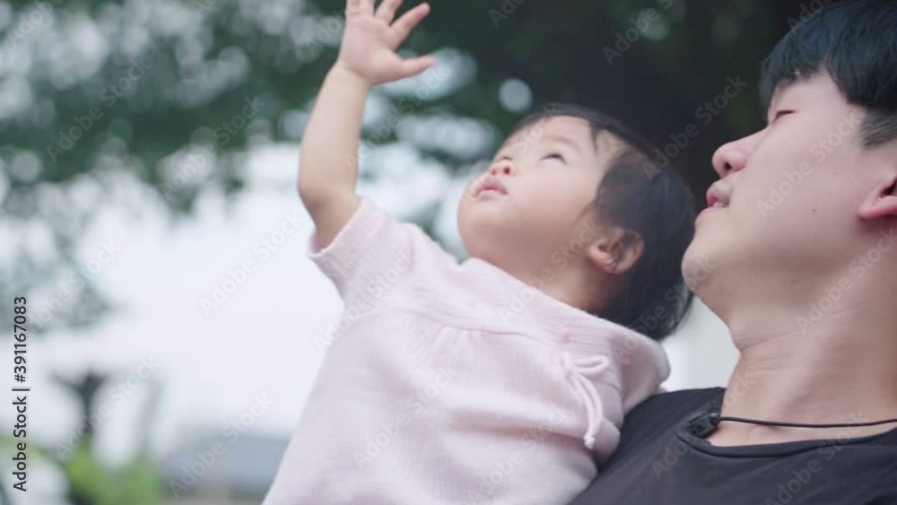 young Asian dad holding his baby girl looking up to the sky waving hand at park under trees, child care parent love bond, children innocence, father and child happy scene, hope for next generation young Asian dad holding his baby girl looking up to the sky waving hand at park under trees, child care parent love bond, children innocence, father and child happy scene, hope for next generation