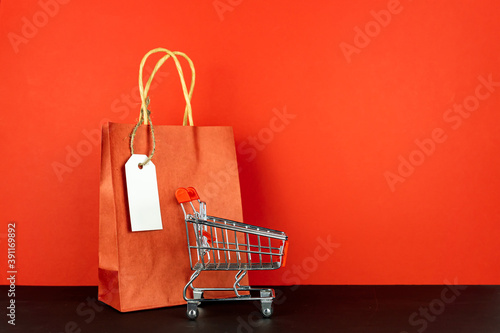 Shopping lover concept : Red paper shopping bags and small toy shopping cart on red background.