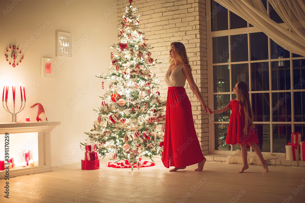 Merry Christmas and Happy Holidays. Mom and daughter with a Christmas tree indoors at night. The evening before Christmas. Portrait of a loving family nearby. High quality photo.