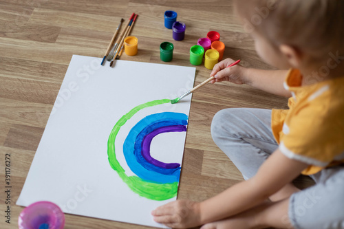 Child painting a rainbow with gouache.