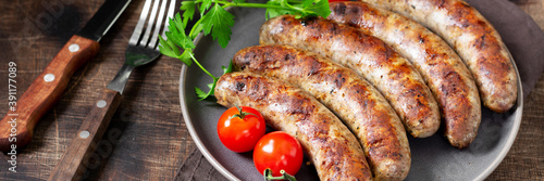 Fried sausages. Grilled sausages with spices, sauce, tomatoes and parsley. Delicious meat sausages in a ceramic plate. Banner	