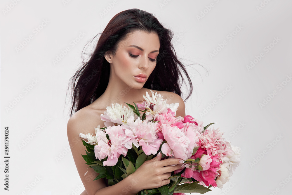 Sexy brunette woman holding a large bouquet of peony flowers. Perfect makeup and beautiful soft skin