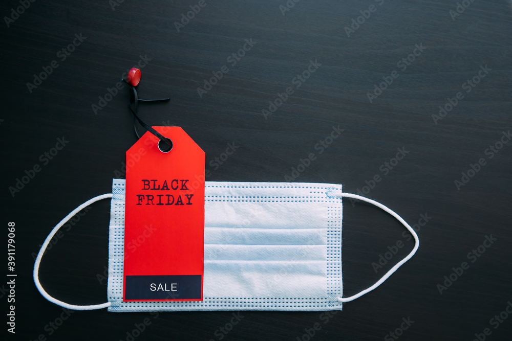 Red tag with the inscription Black Friday on the background of medical mask. Sales in the context of Covid-19 pandemic. Concept of safe shopping.
