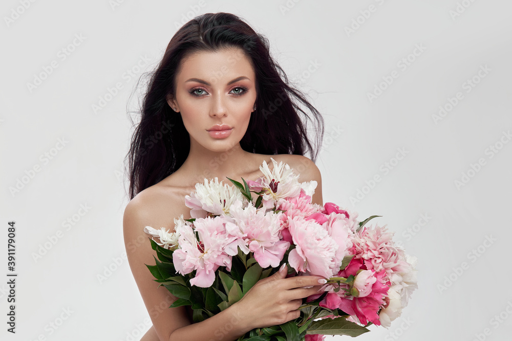 Sexy brunette woman holding a large bouquet of peony flowers. Perfect makeup and beautiful soft skin